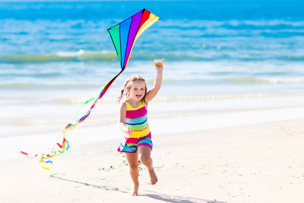 Girl smiling and running with a kite on the beach.