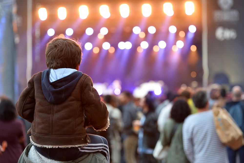 Kid sitting on a parent's shoulders at a concert
