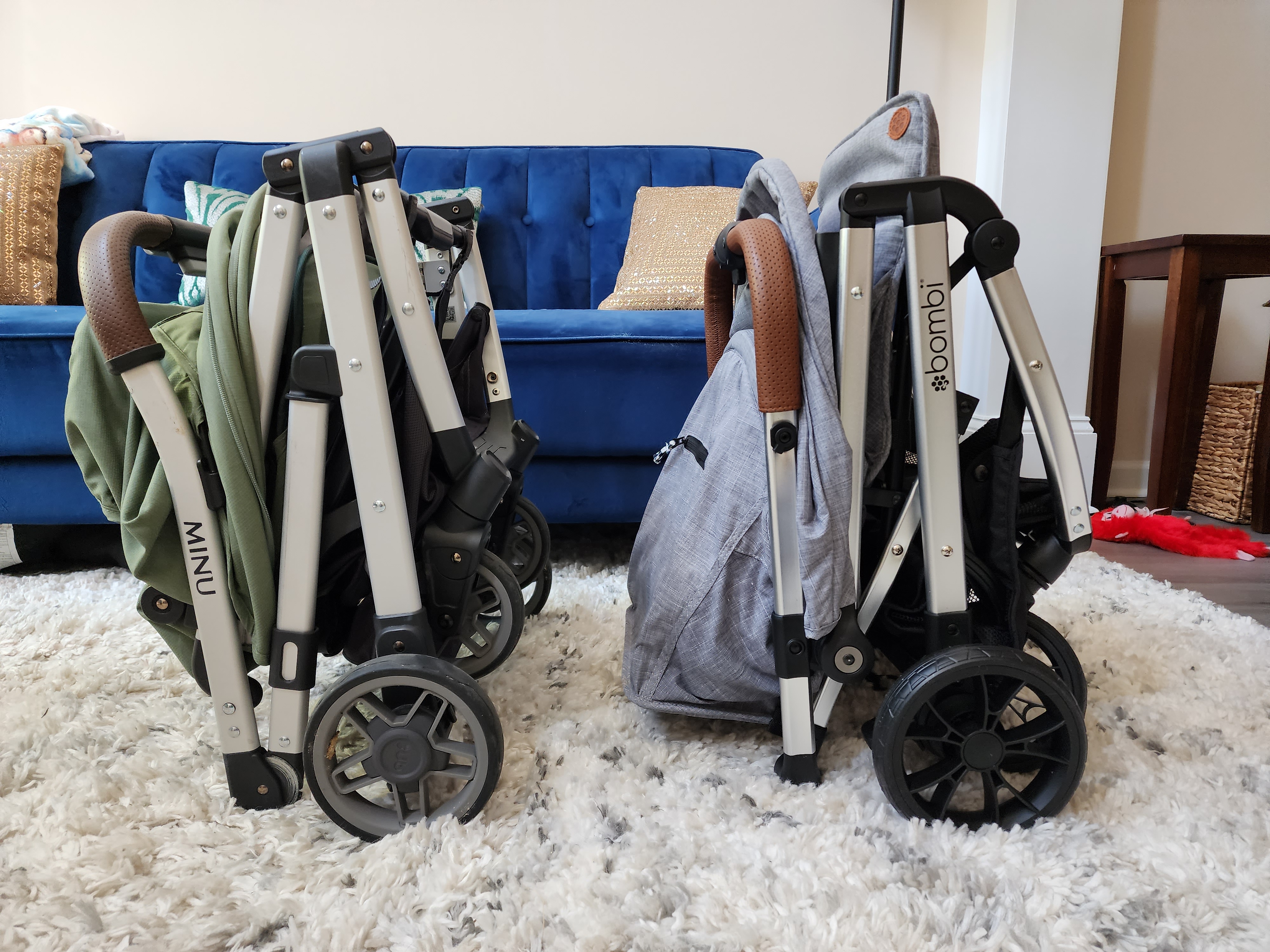two travel strollers folded up in a living room side by side