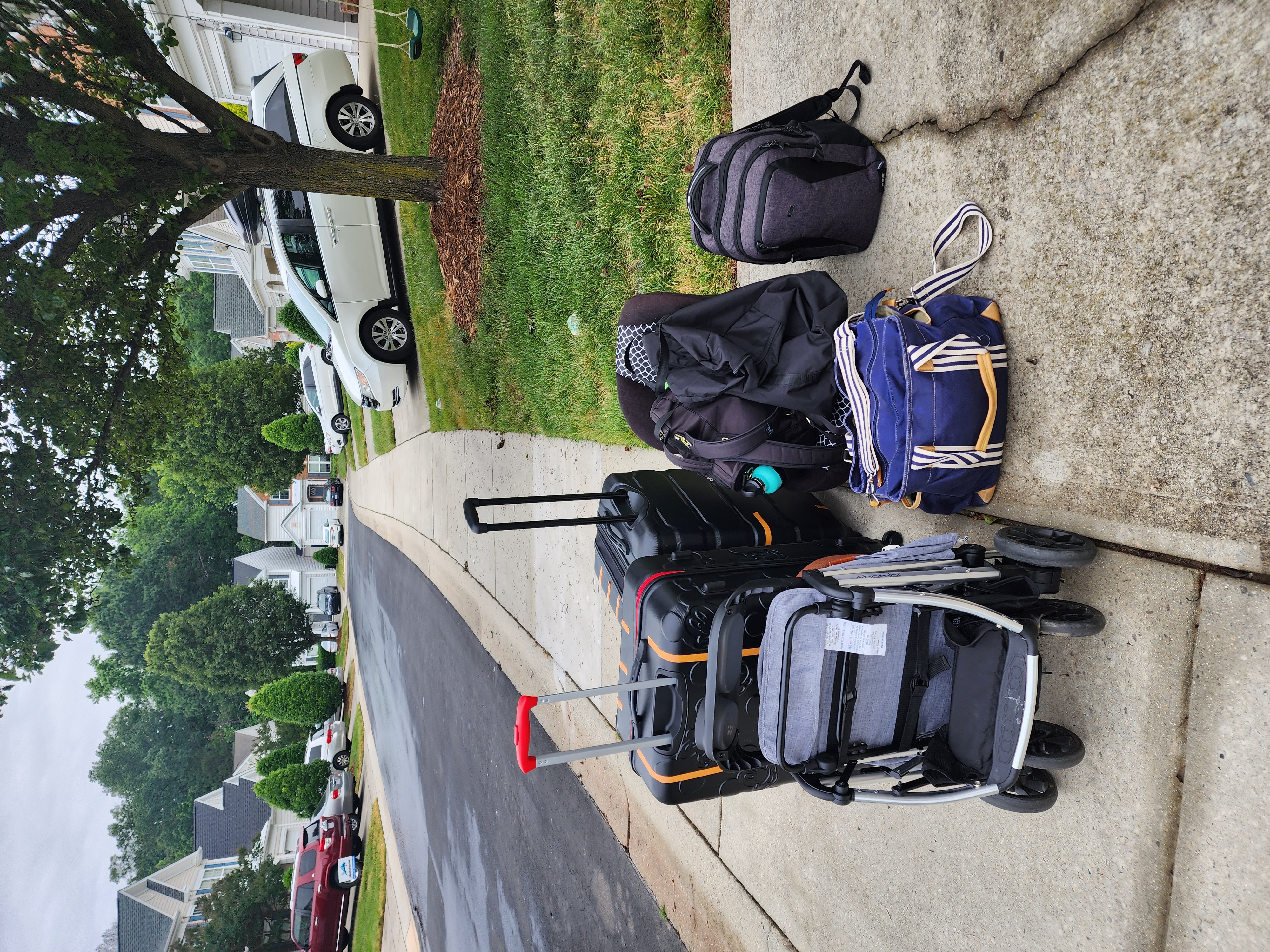 a group of suitcases bags and a stroller are sitting on a sidewalk in a neighborhood